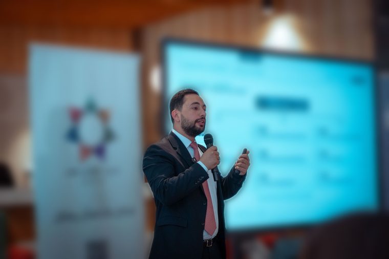 Salem Ababneh speaking with a microphone, sharp against a softly blurred conference backdrop.